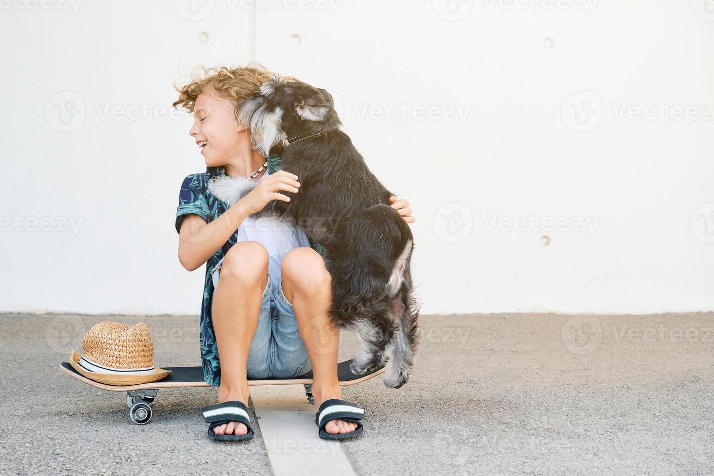 Dog licking face of boy sitting on skateboard photo