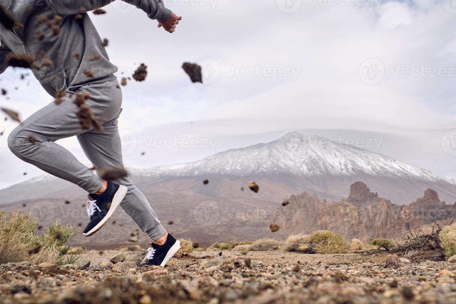 Crop man in activewear running on dirty terrain near mountains photo