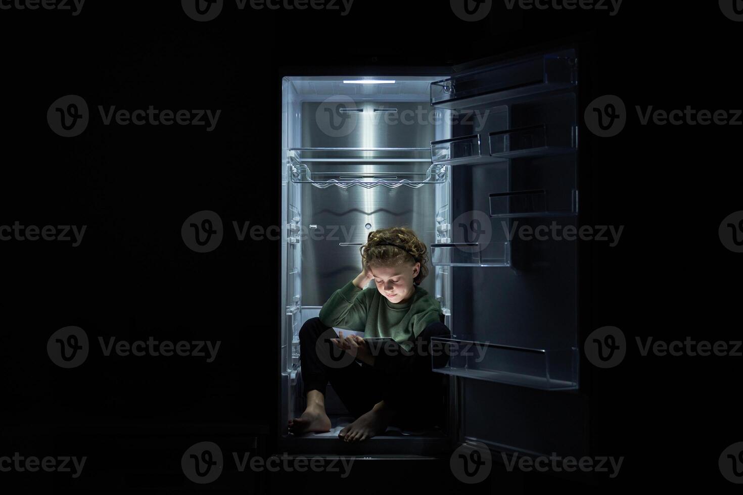 Focused kid watching movie on tablet while sitting in fridge photo