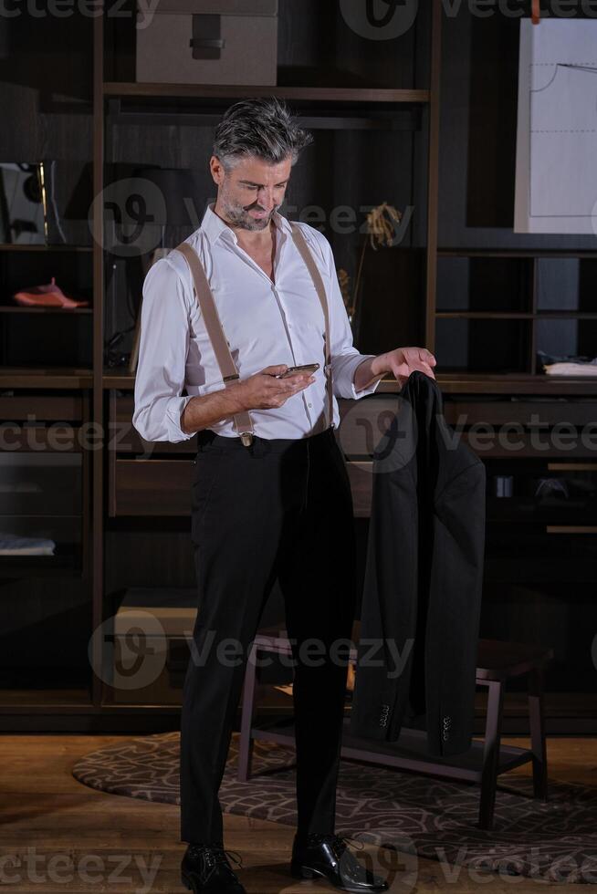 Middle aged elegant man checking message on phone in wardrobe photo