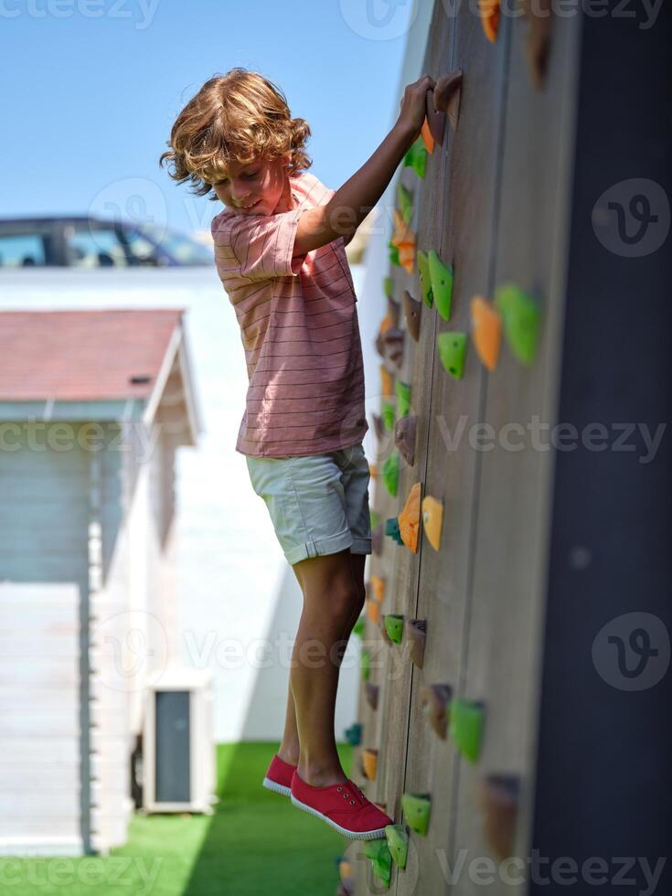 Little boy climbing wall while looking down photo