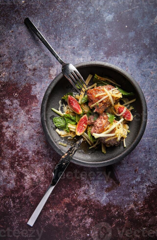 Pig trotter with figs and vegetables with greenery on plate photo