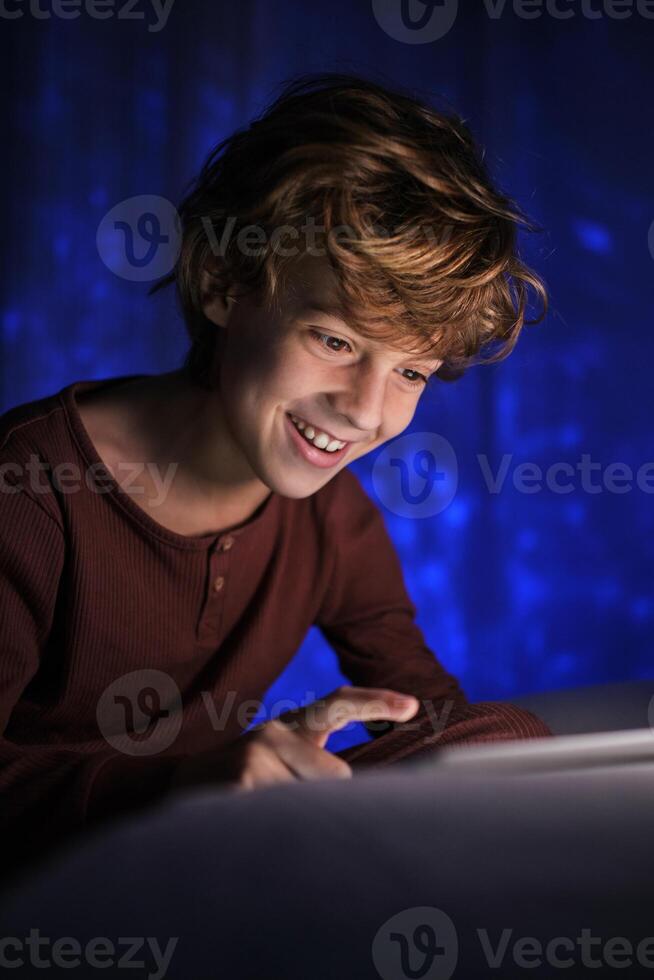 Smiling boy using tablet in dark room photo