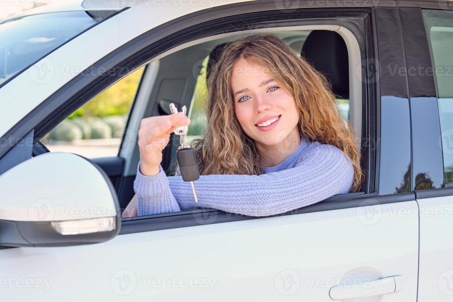 Cheerful woman showing keys and sitting in car photo