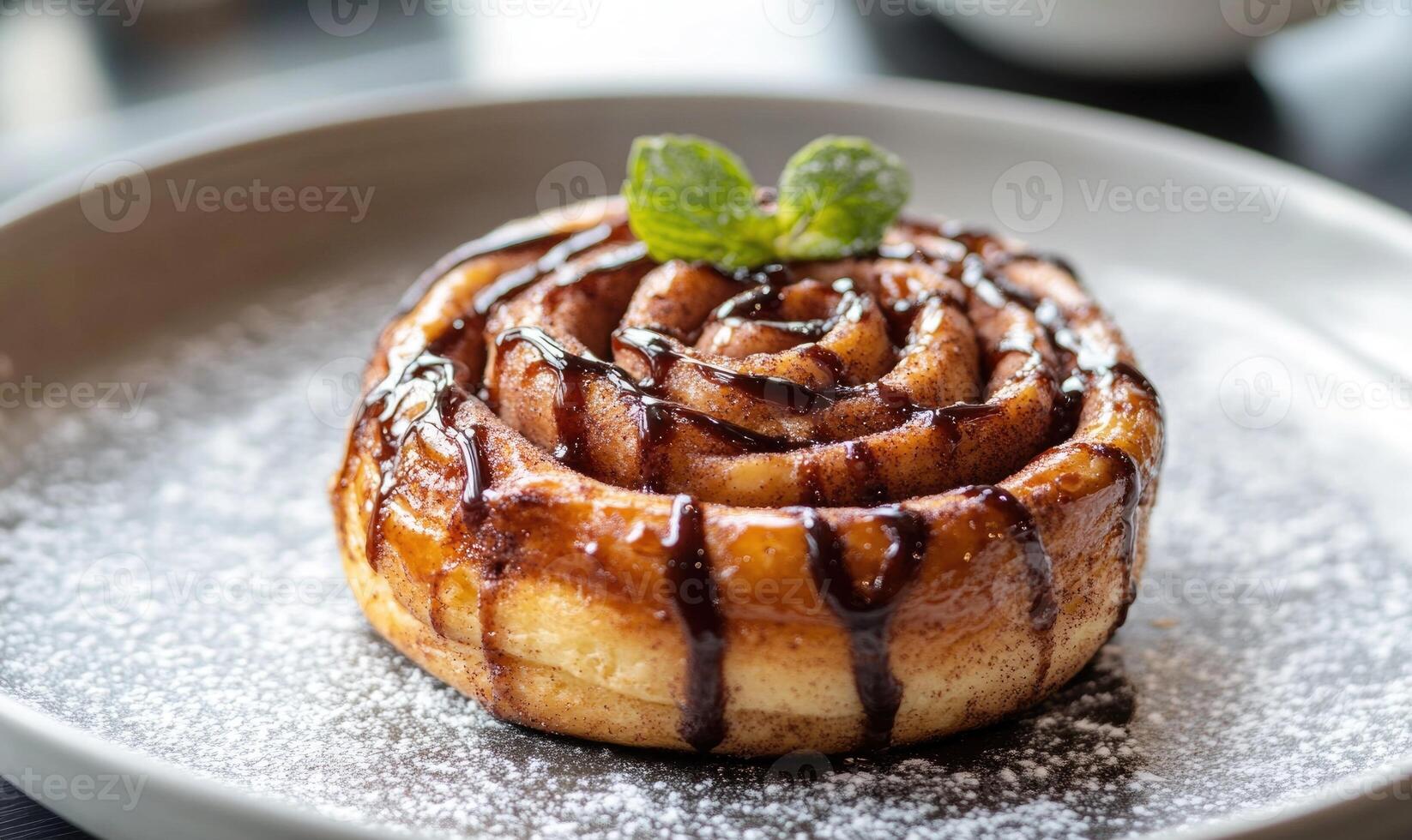 A cinnamon roll with chocolate syrup and a green leaf on top photo
