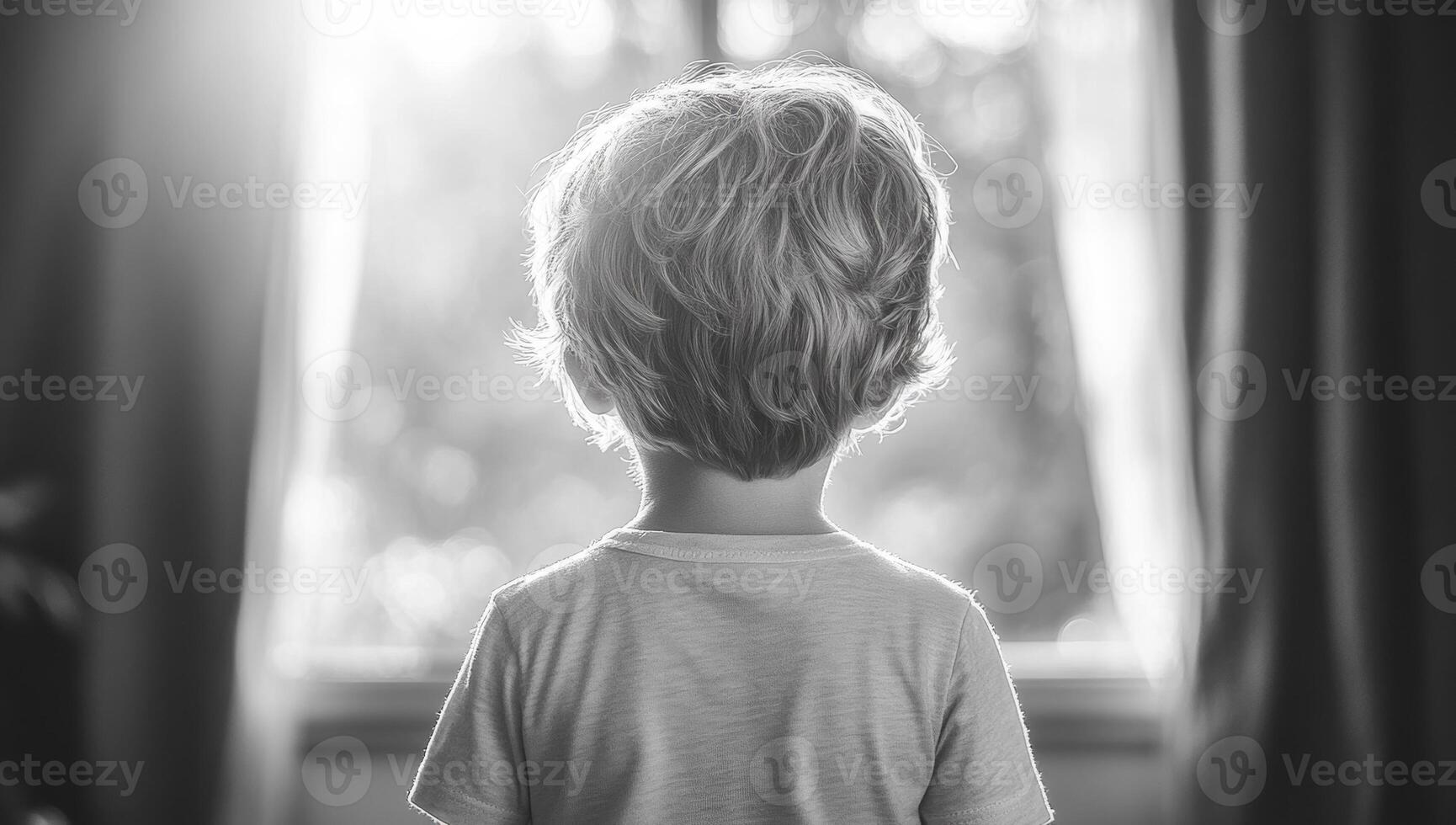 Child gazing out of window in sunlight. A young child stands silently, looking out of a sunlit window, deep in thought as light filters through. photo