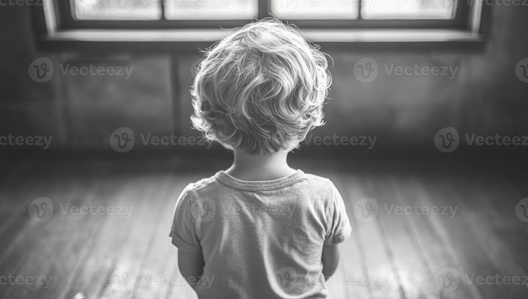 Child gazing out a window. A young child with curly hair stands quietly, looking out a large window in a softly lit room, lost in thought. photo