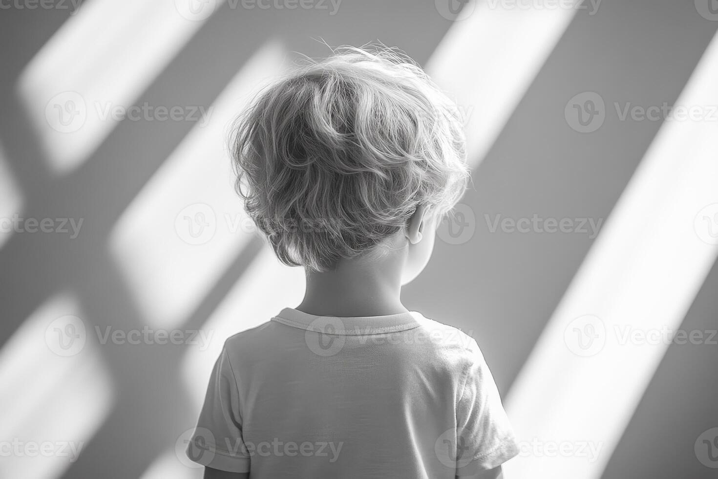 Child gazing in soft light shadows. A child stands quietly, gazing thoughtfully as sunlight casts soft shadows across the wall. photo