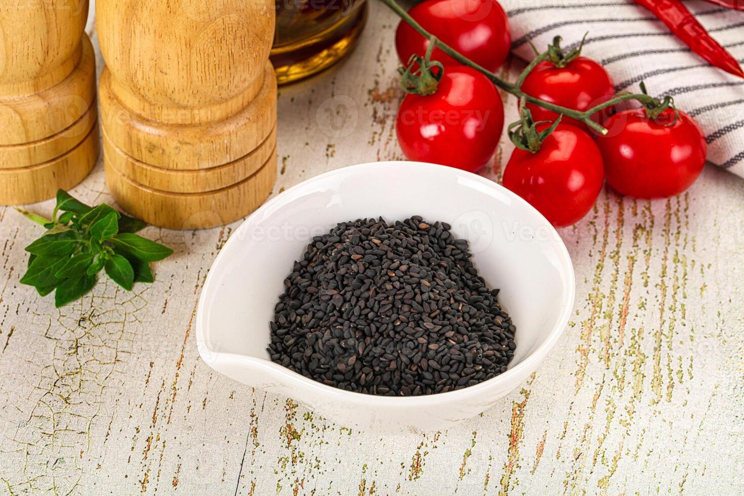 A bowl of black seeds on a table next to a bottle of olive oil photo