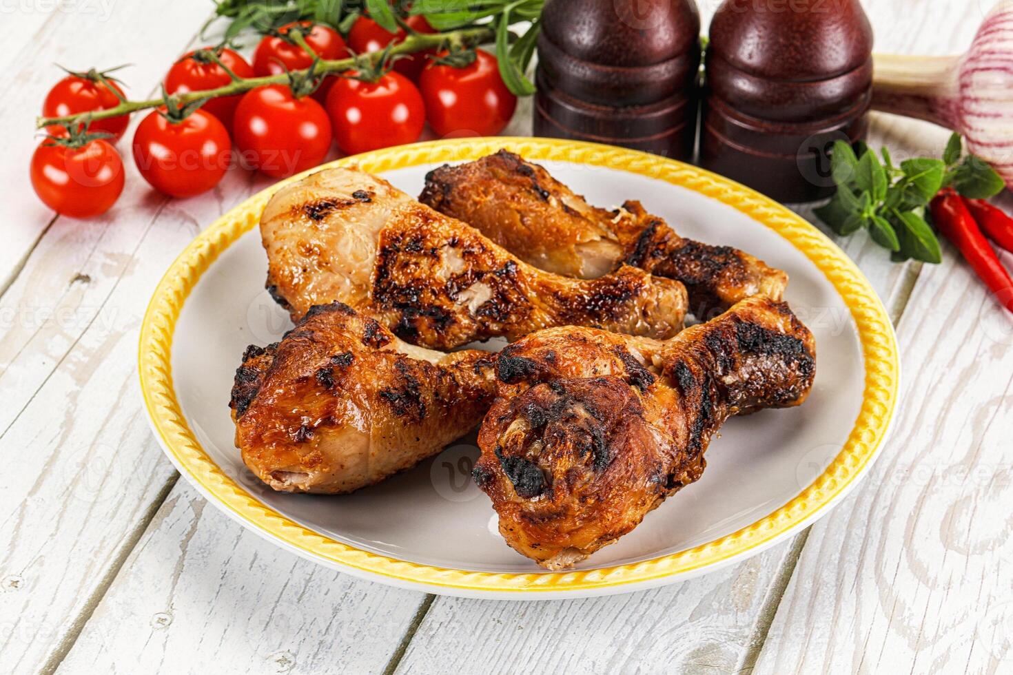 A plate of chicken legs on a table with tomatoes and peppers photo