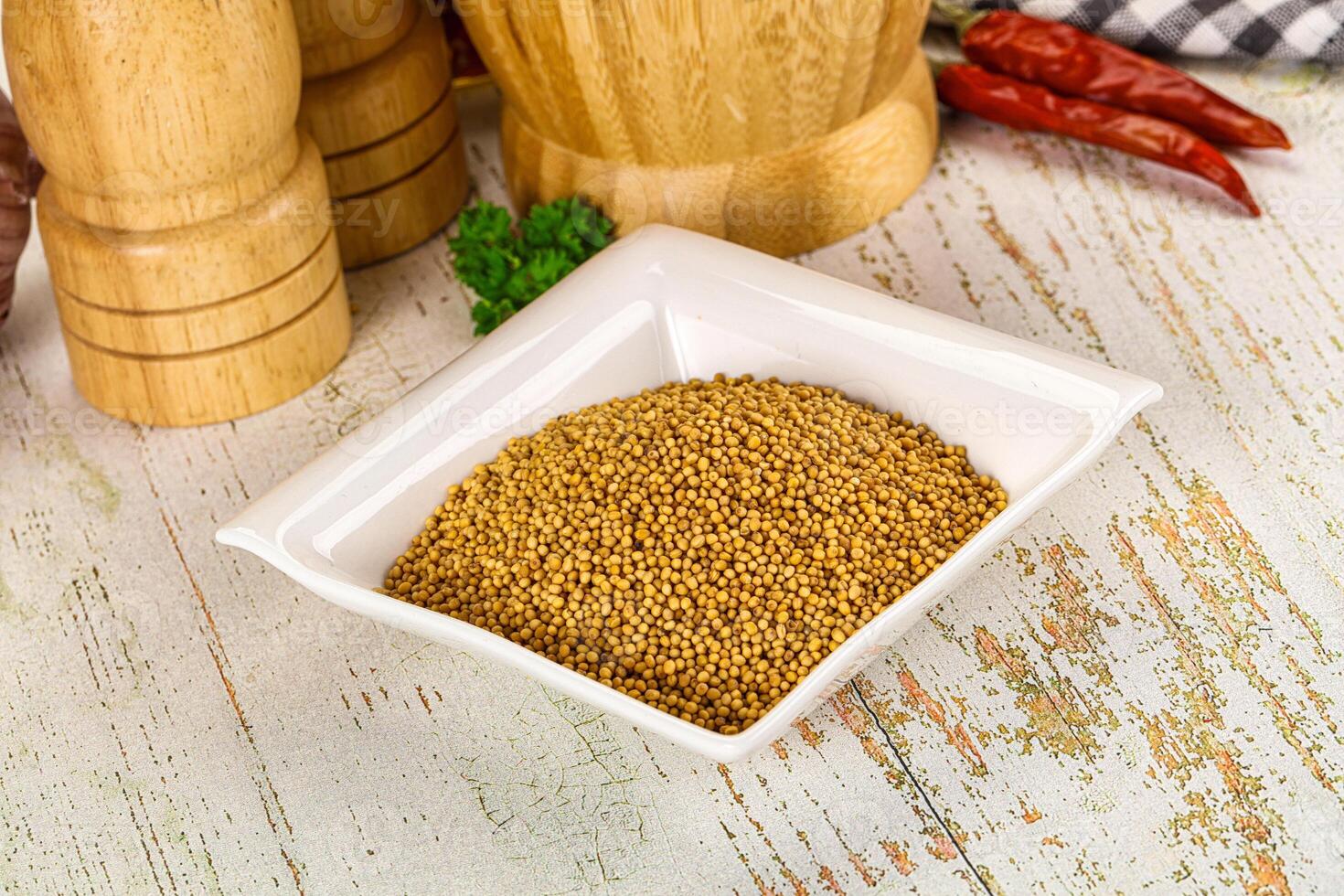 A bowl of mustard seeds and spices on a wooden table photo
