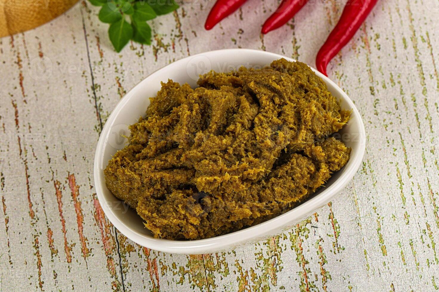 A bowl of green paste with chili peppers on a wooden table photo