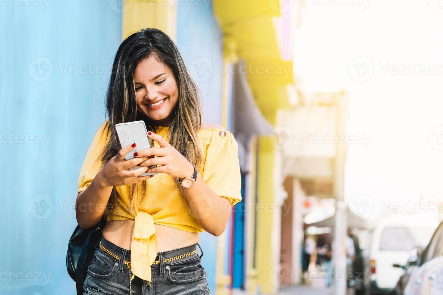 portrait of a cheerful young Asian woman walking down the street typing a text message from a smart phone. mobile applications concept. photo