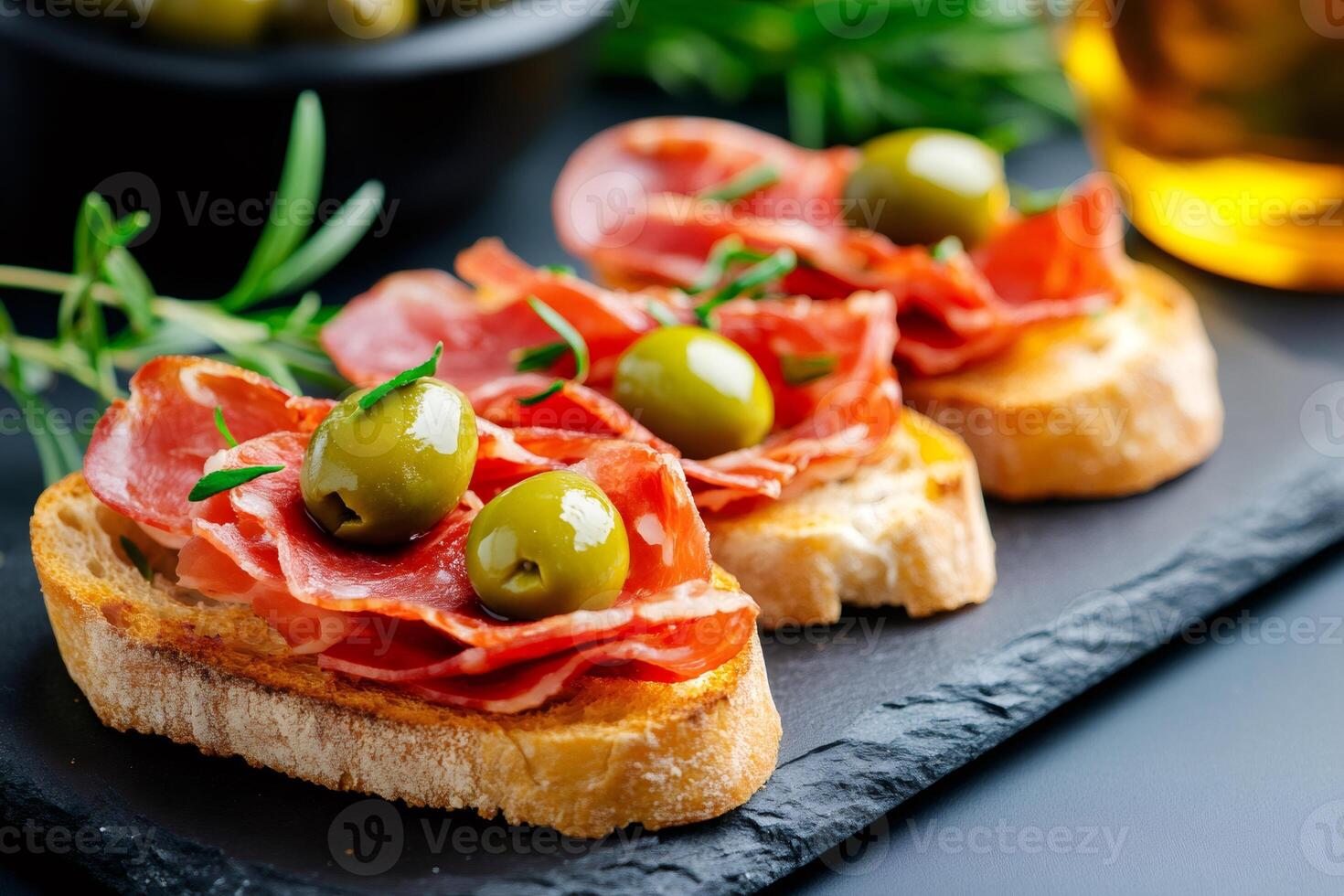 Delicious bruschetta with salami, olives and rosemary lying on black stone plate photo