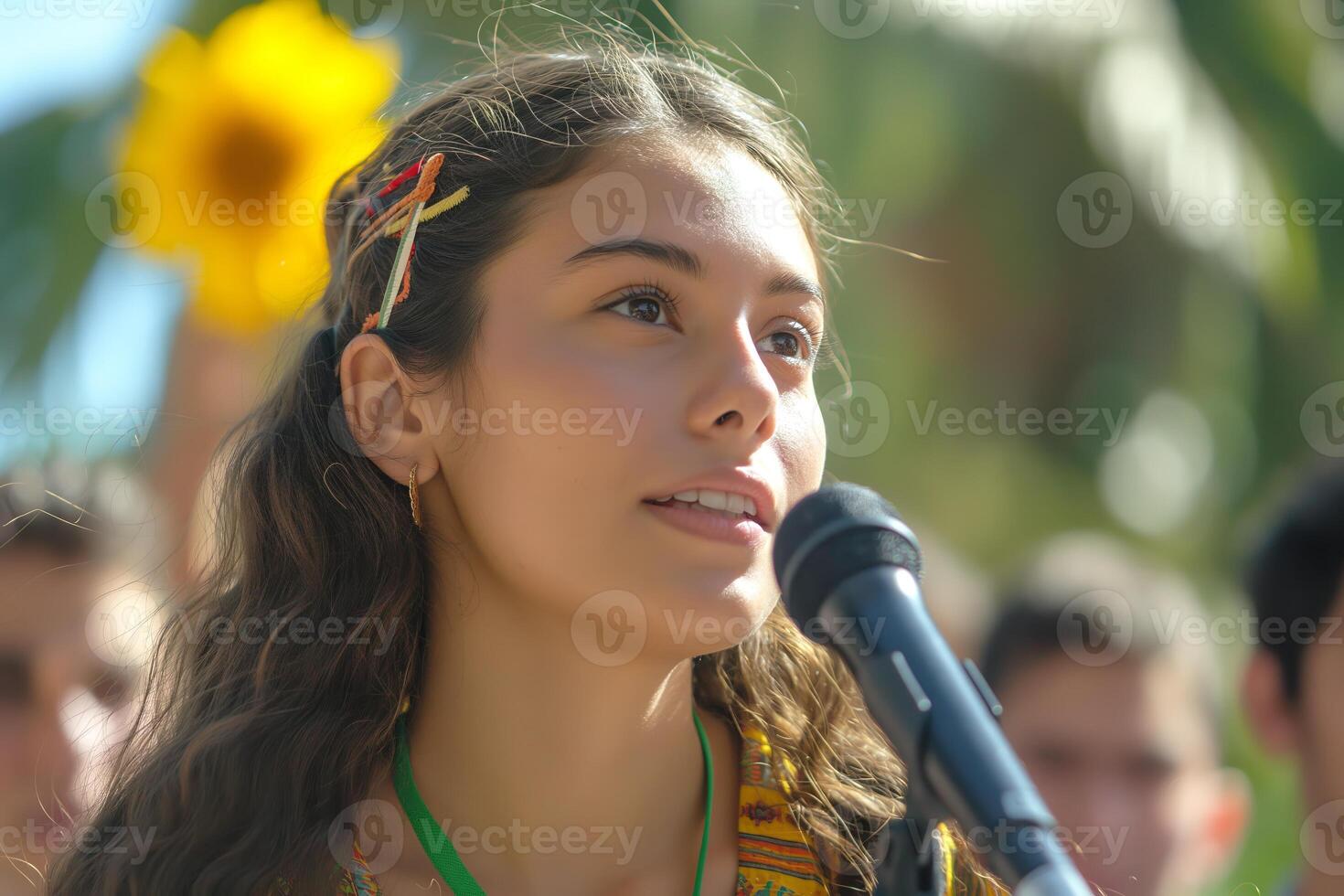 A young Latina girl passionately speaks into a microphone at a vibrant outdoor event, surrounded by enthusiastic supporters. photo