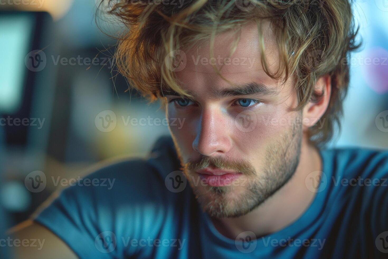 Close-up portrait of a young Caucasian man with tousled hair, deep blue eyes, and a pensive expression, captured in soft lighting. photo