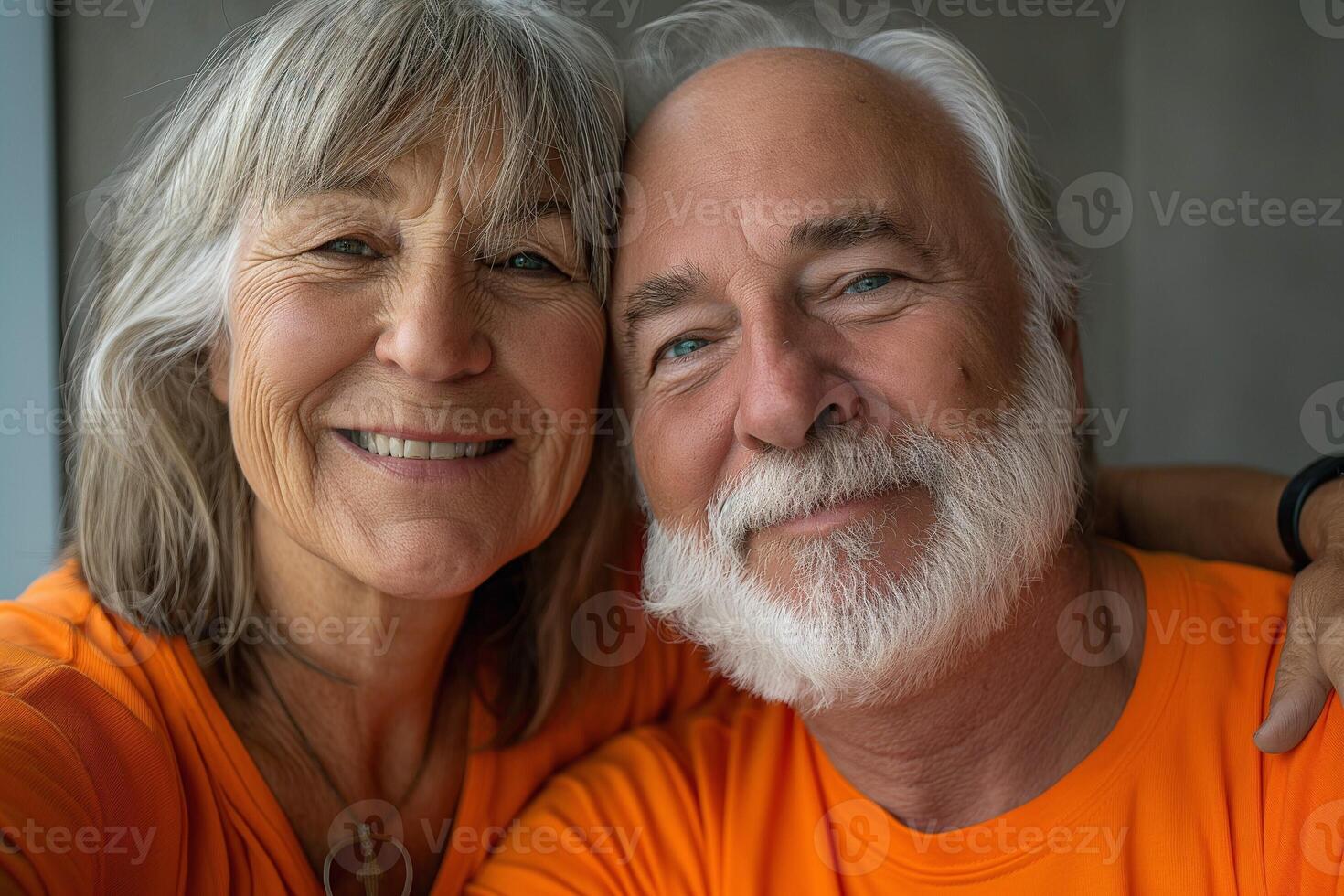 A joyful senior couple smiling together in matching orange shirts, exuding warmth and love. photo