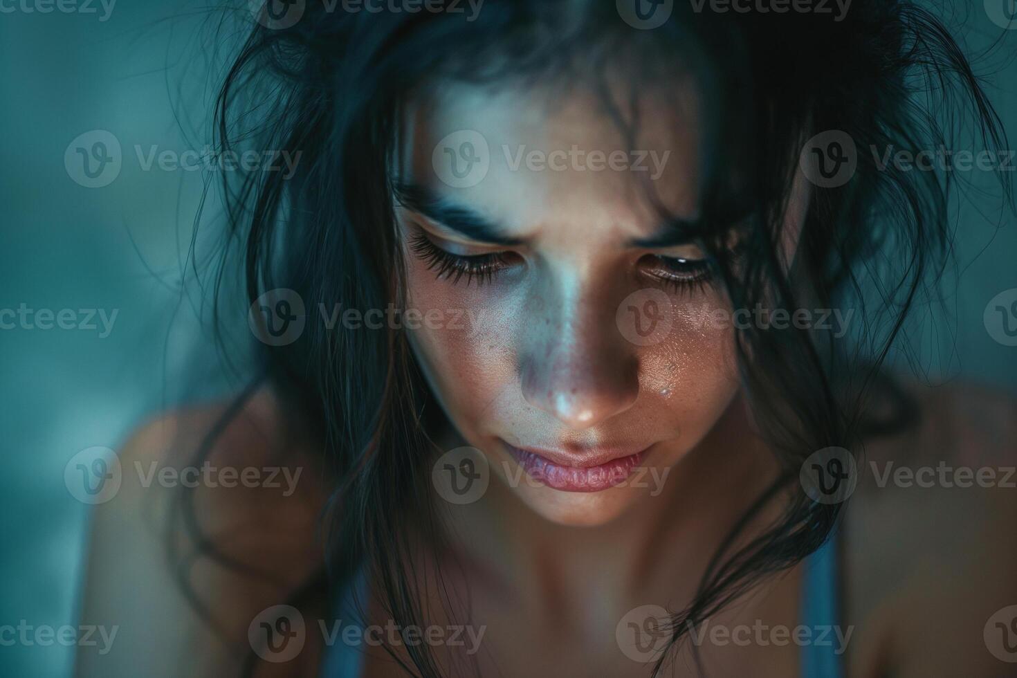 A young Latina woman with long, dark hair gazes downward, deep in thought, her expression conveying a mix of emotion and contemplation. photo