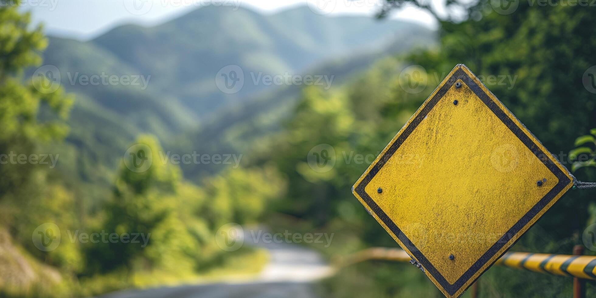 A yellow warning sign stands by a winding road, surrounded by lush greenery and distant mountains. photo