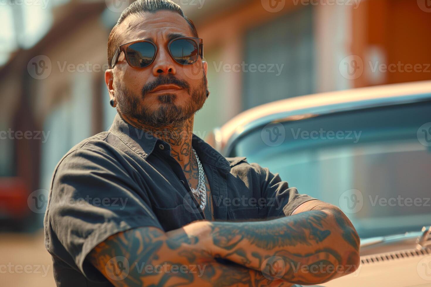 A confident Latino man with tattoos stands by a vintage car, exuding a cool, relaxed vibe under the warm sunlight. photo