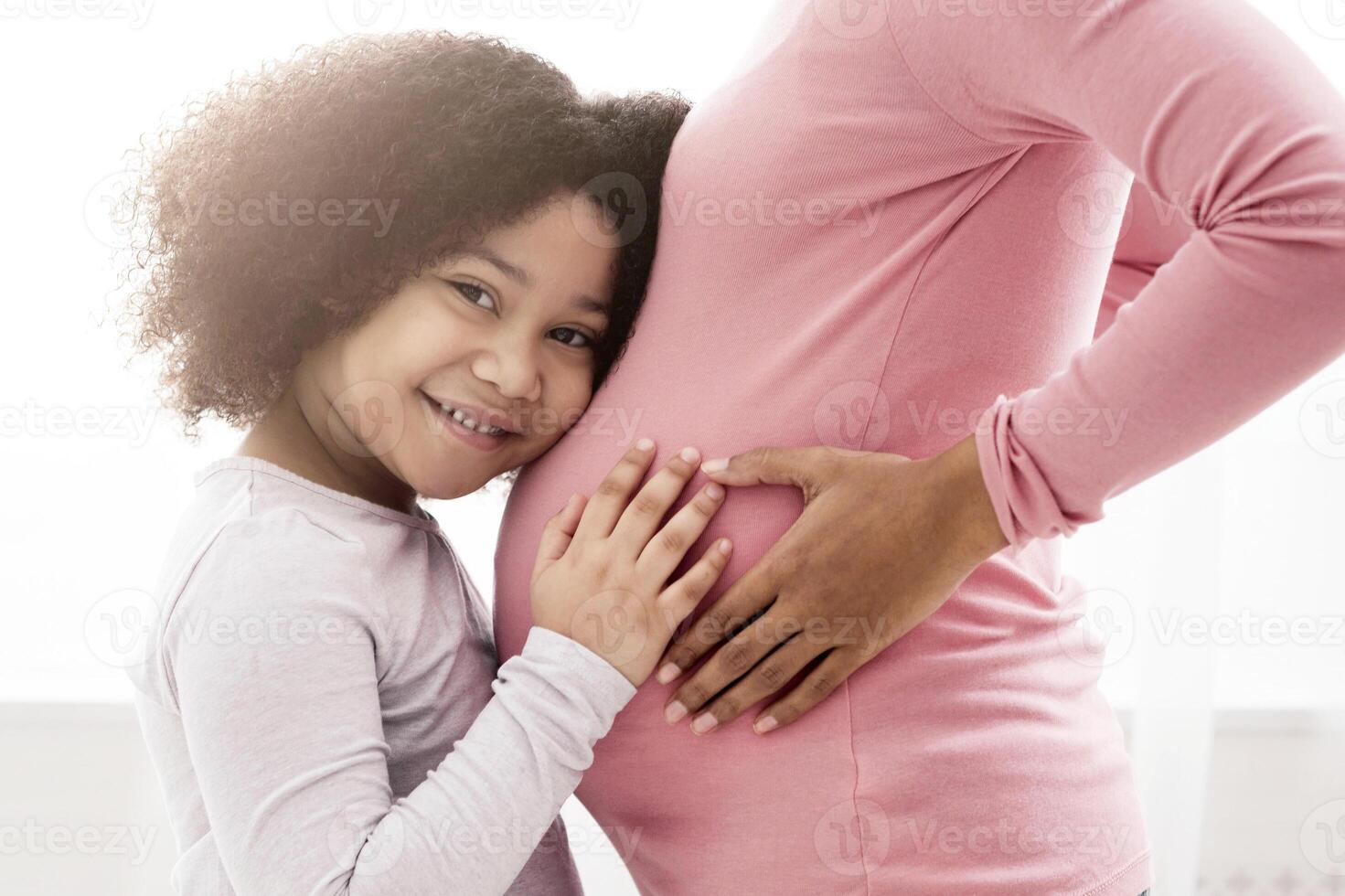 Happy Expectation. Cute Little Afro Girl Cuddling Mother's Pregnant Belly, Awaiting For Her Sibling To Born, Crop, Free Space photo