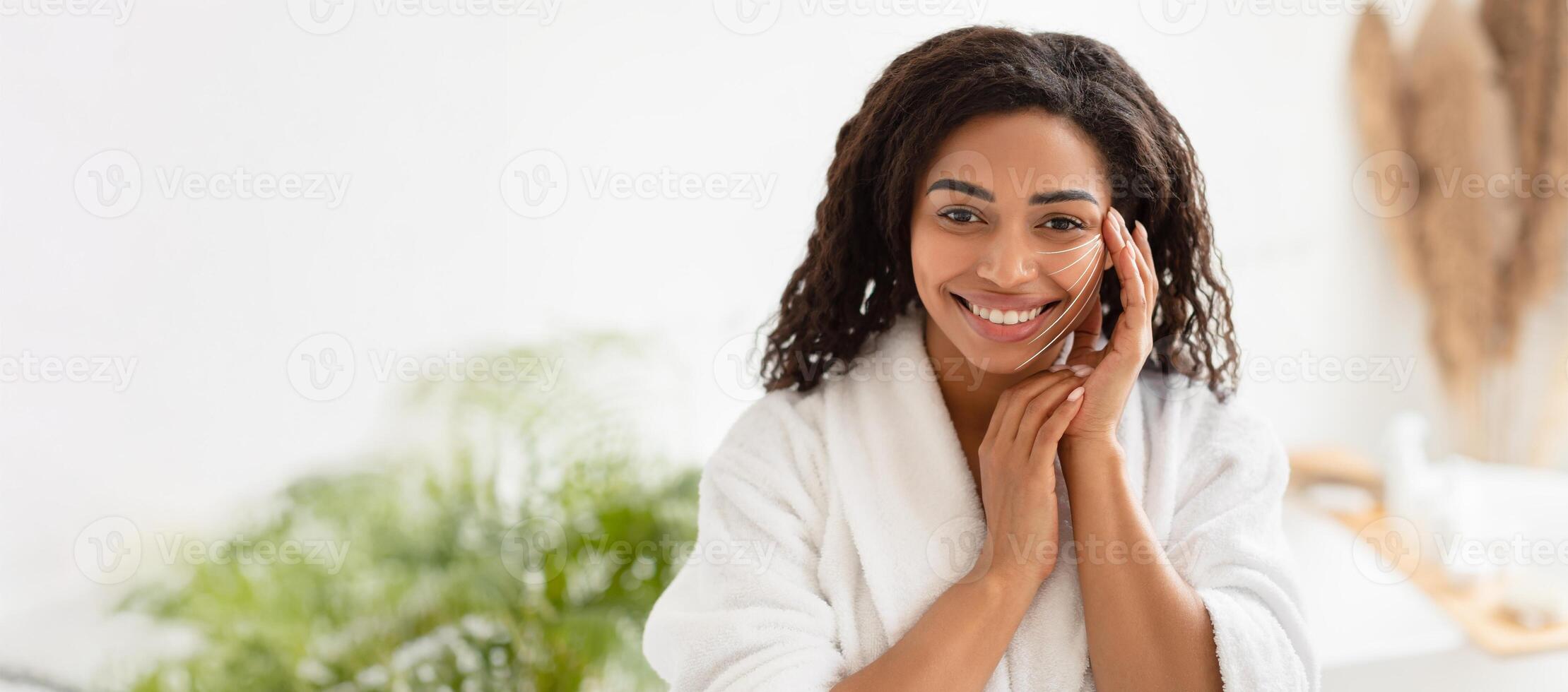 African American woman relaxes in a spa, applying skincare products. She smiles while pampering herself, embodying the essence of self-care and anti-aging in a calming environment. photo