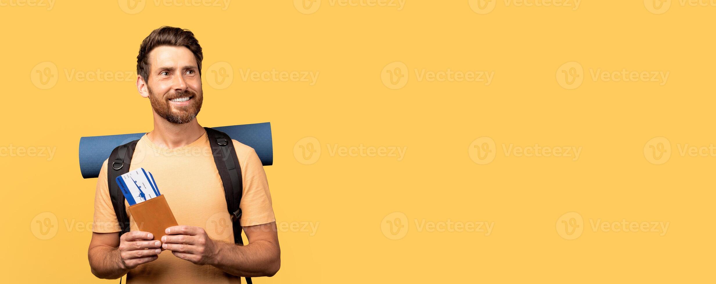 A happy millennial man traveler stands with a backpack and travel documents, wearing a bright shirt against a bold yellow background. They are ready for the upcoming holiday adventure. photo