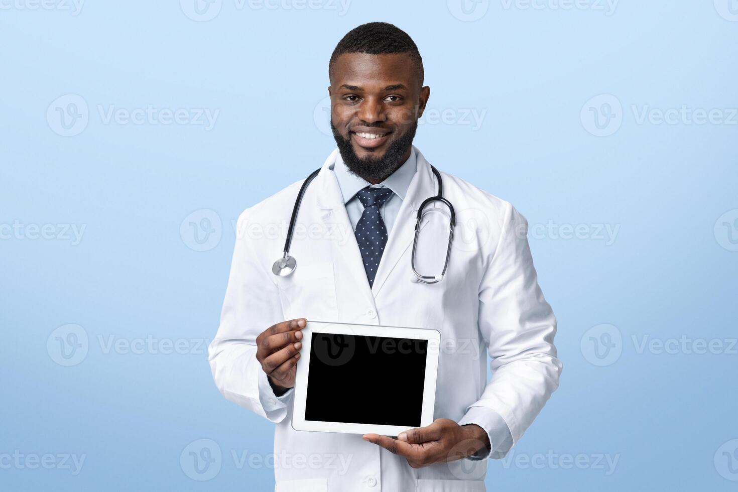 Positive black therapist holding digital tablet with empty screen, recommending online application for healthcare, white studio background photo