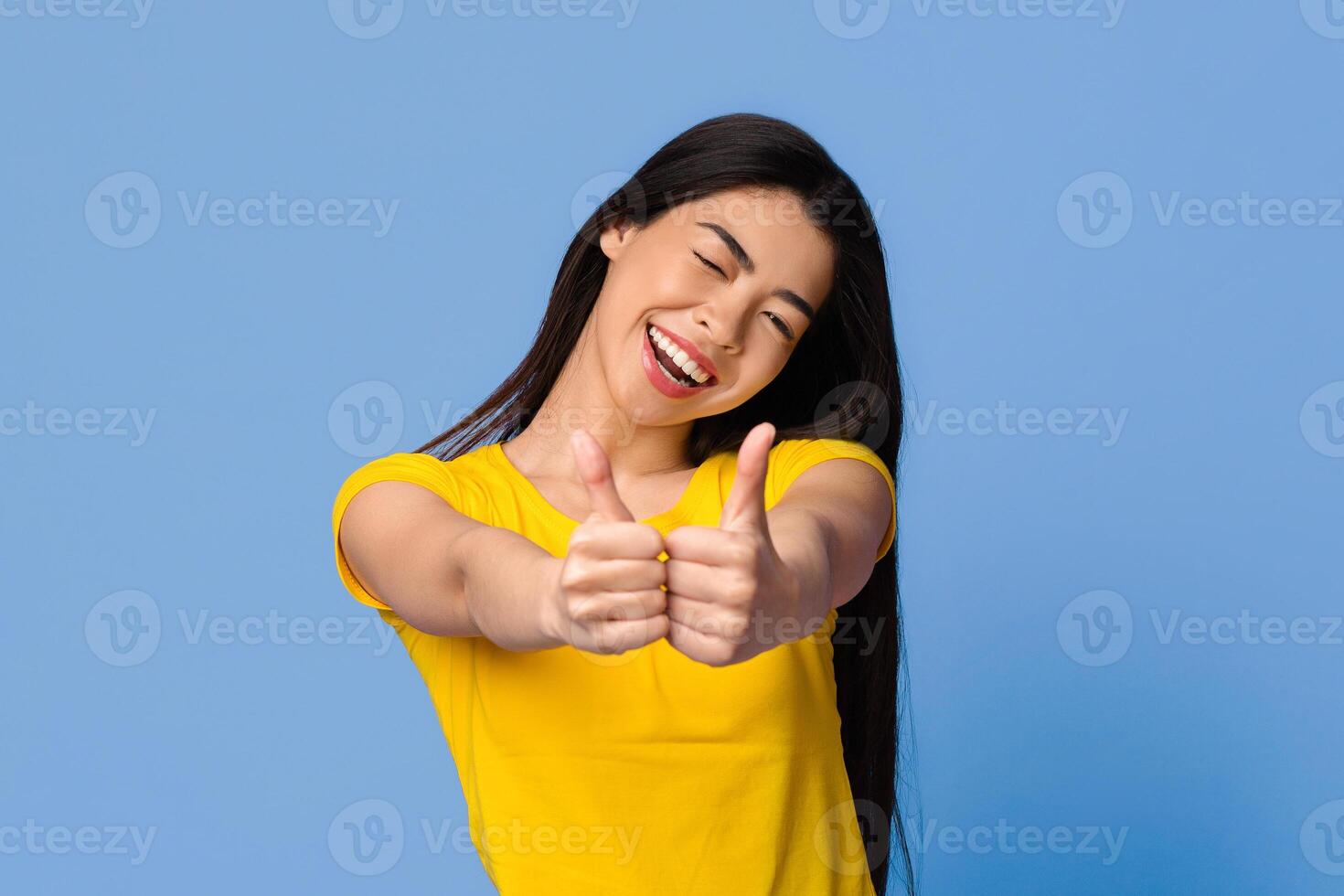 I Like It. Joyful Young Asian Woman Showing Thumbs Up With Both Hands And Winking At Camera, Positive Korean Lady Recommending Something, Gesturing Sign Of Approval, Posing Over Purple Background photo