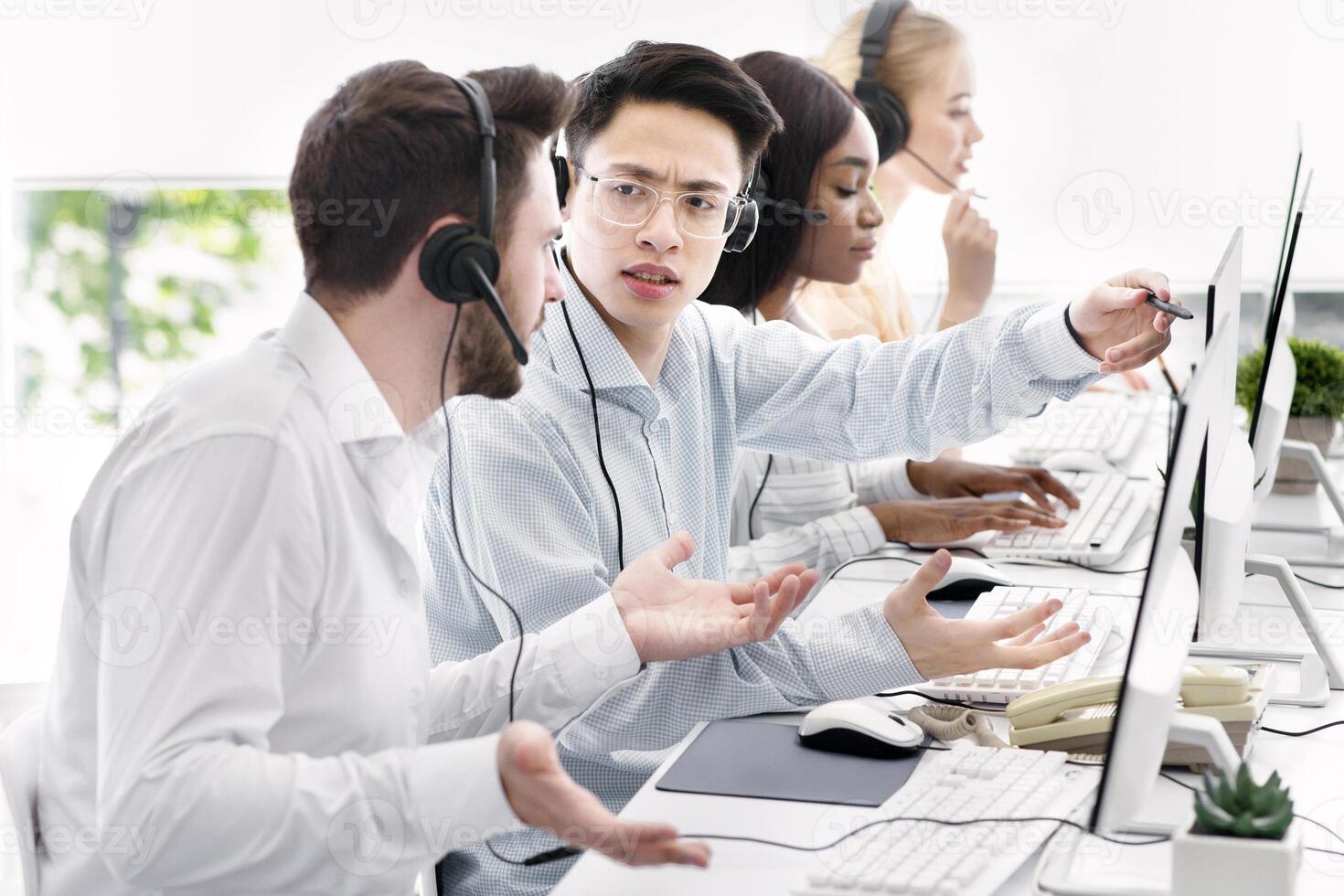 User support service concept. Hotline operator helping his coworker at call centre. Customer care agents communicating to each other, solving client's problem at modern office photo