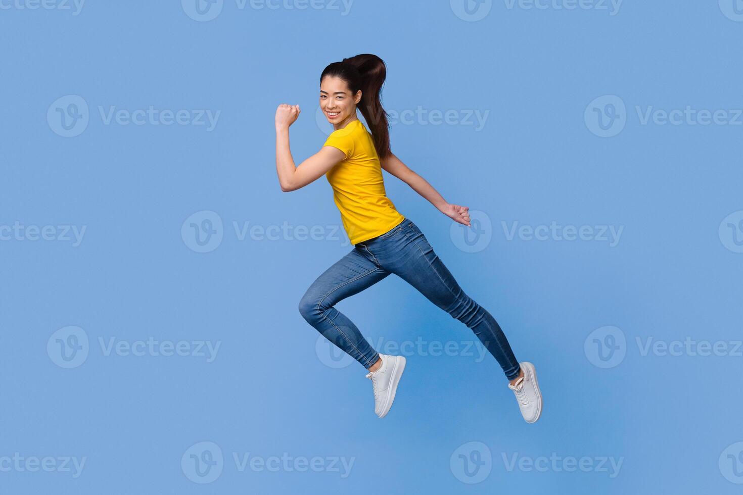Time To Move. In Motion Portrait Of Happy Asian Girl Jumping In The Air Over Purple Background, Full-Length Shot With Copy Space photo