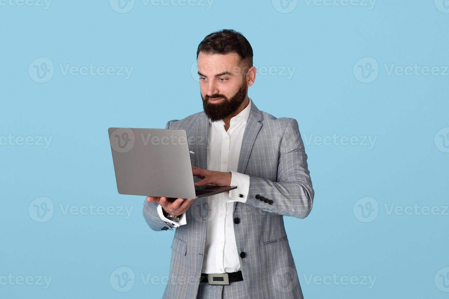 Online business concept. Confident young entrepreneur using laptop computer for remote work or communication, watching educational webinar, having meeting on blue studio background photo