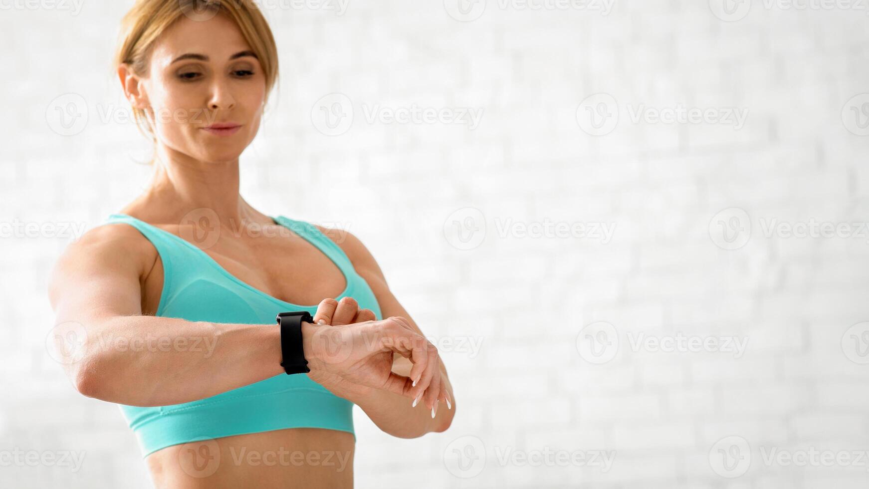 Training result. Muscular adult woman in sportswear looks at smart watch on hand and checks biological rhythms, copy space photo