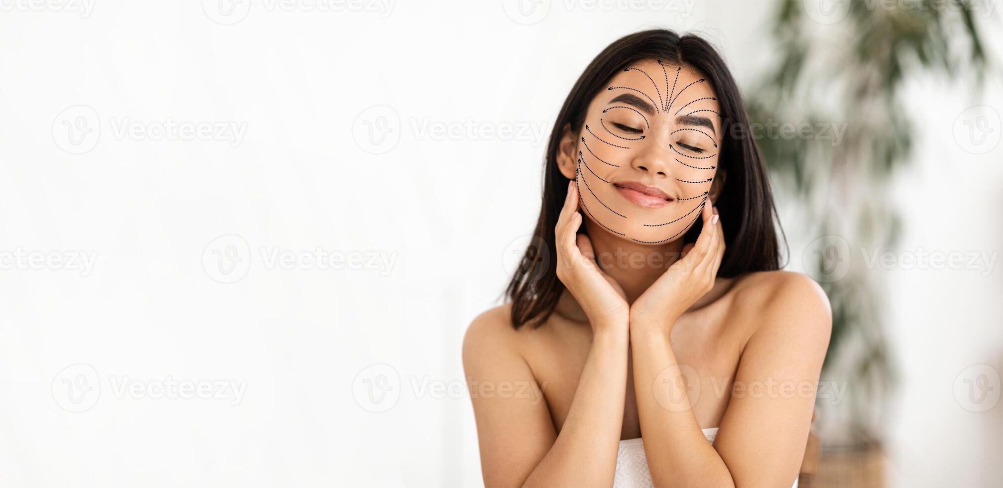 Asian woman is pampering herself with a skincare treatment, smiling contentedly while getting a facial massage. She is in a bright, serene skincare studio designed for relaxation and rejuvenation. photo