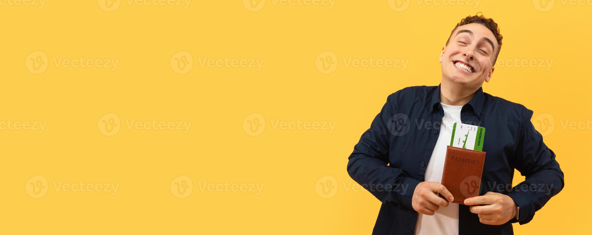 Overjoyed blonde handsome young guy tourist showing passport with flight tickets, boarding pass and grimacing, going vacation, isolated on yellow background, copy space photo