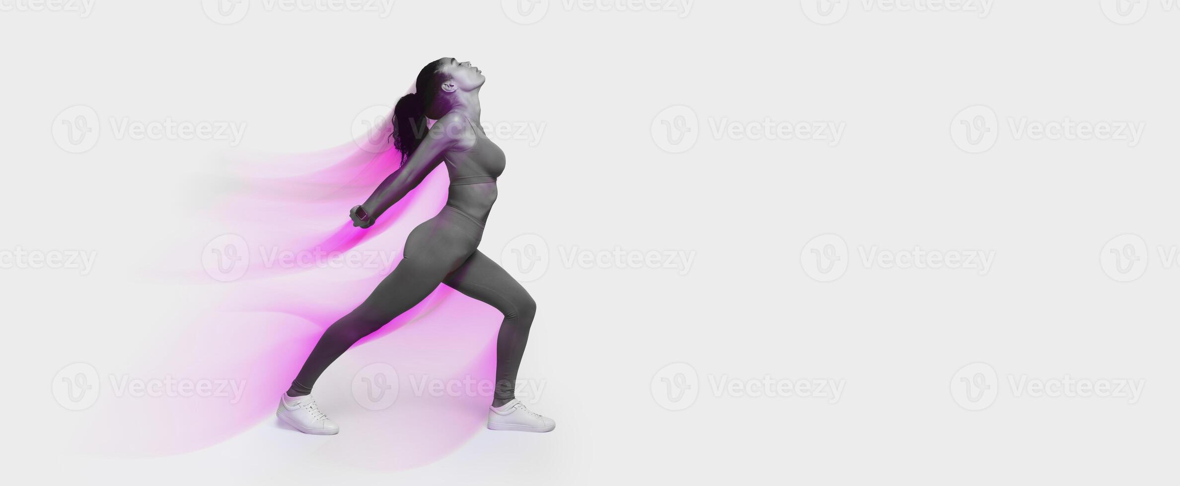 Young African American woman in fitwear performing backbend in lunge position, stretching back muscles in bend, over pink studio backdrop. Fitness routine and workout in gym. Full length photo