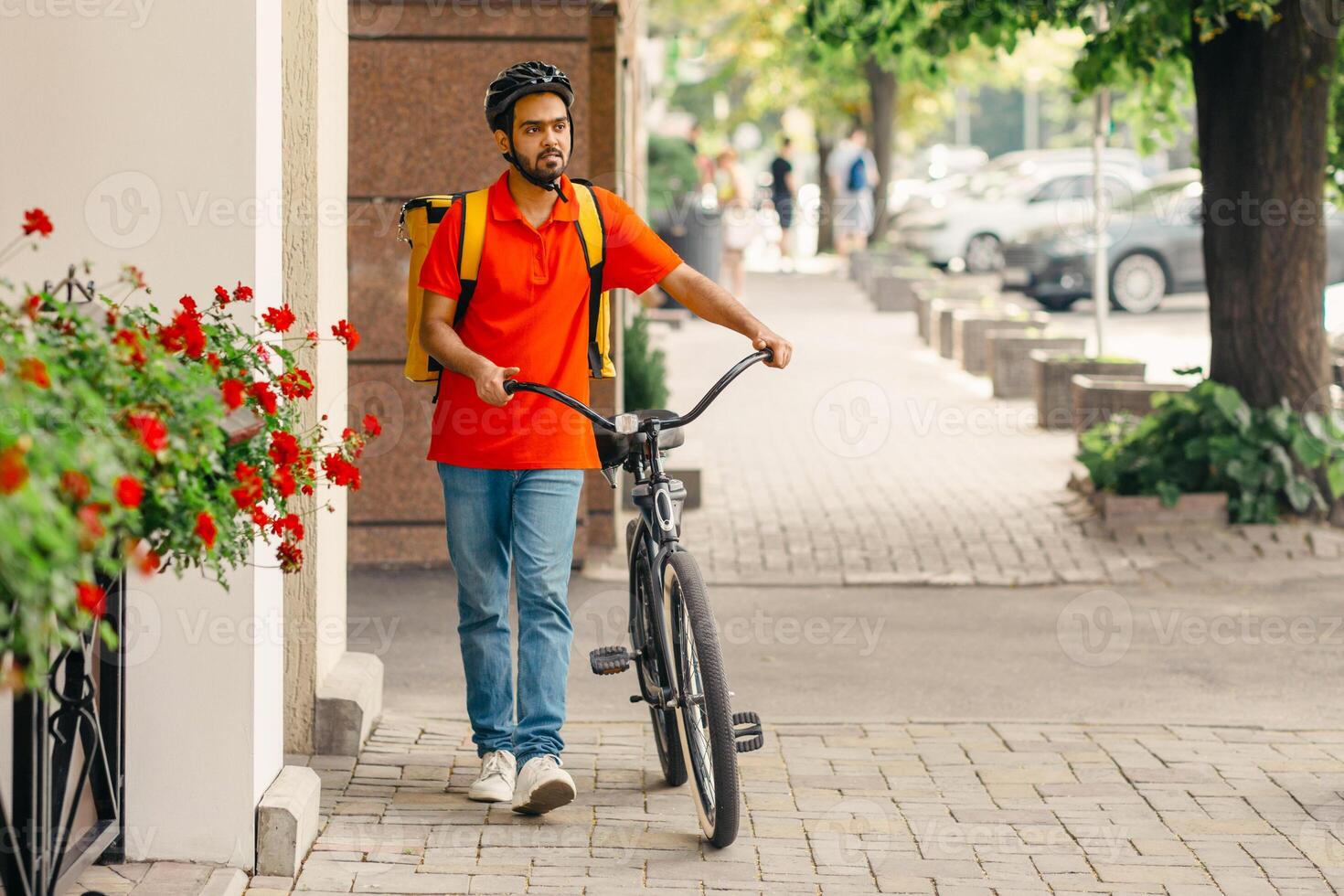 Green city and ecological transport. Courier with beard, helmet and yellow bag, walks with bicycle down the street, copy space photo