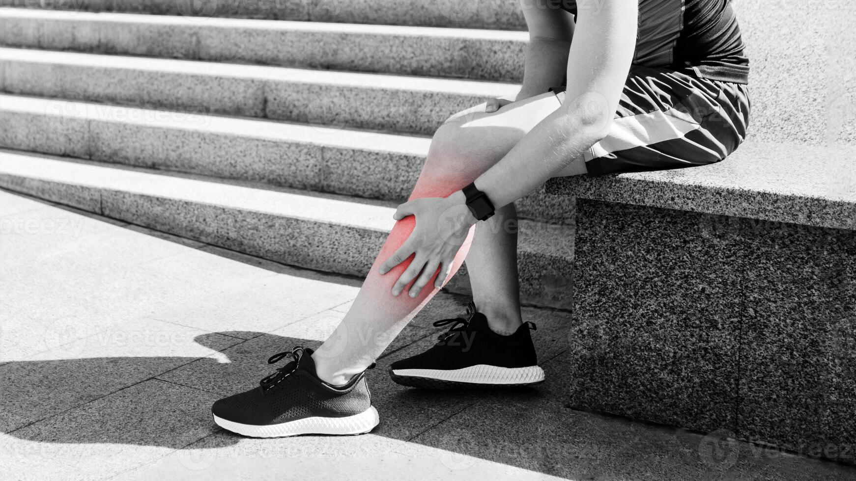 Leg injury while jogging. Guy with expression of pain on face, sits and rubs leg on street, free space photo