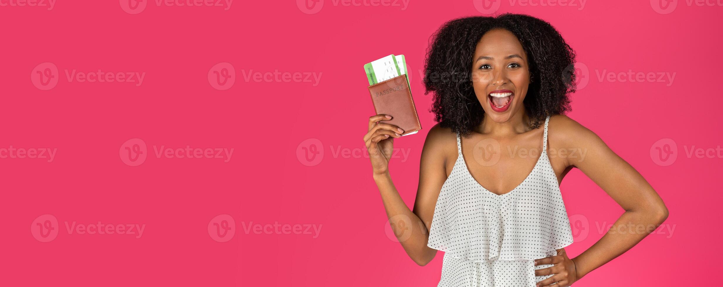 Cheerful surprised young African American curly lady showing passport and tickets, enjoy travel isolated on pink background, studio. Vacation, ad and offer, fun in spare time, trip, adventure photo