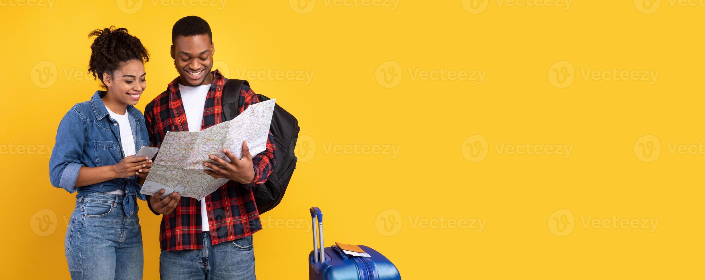 Happy African American Travelers Couple Planning Vacation Using Smartphone And Tourist Map Choosing Destination For Trip Standing On Yellow Studio Background. Travel Application For Tourists Concept photo