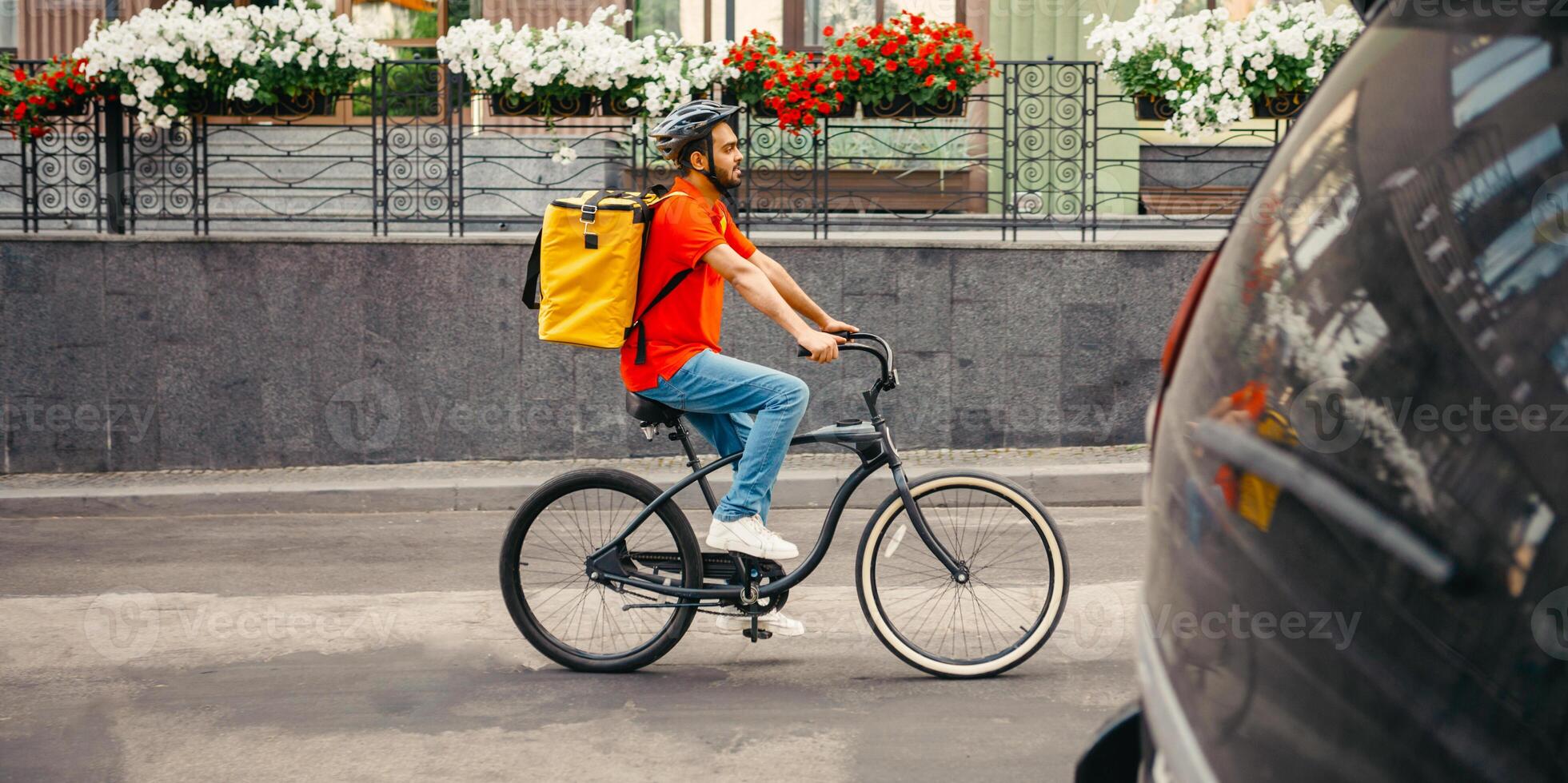 Working day courier in city. Young man in safety helmet with big yellow backpack rides on bicycle at road, side view, free space photo