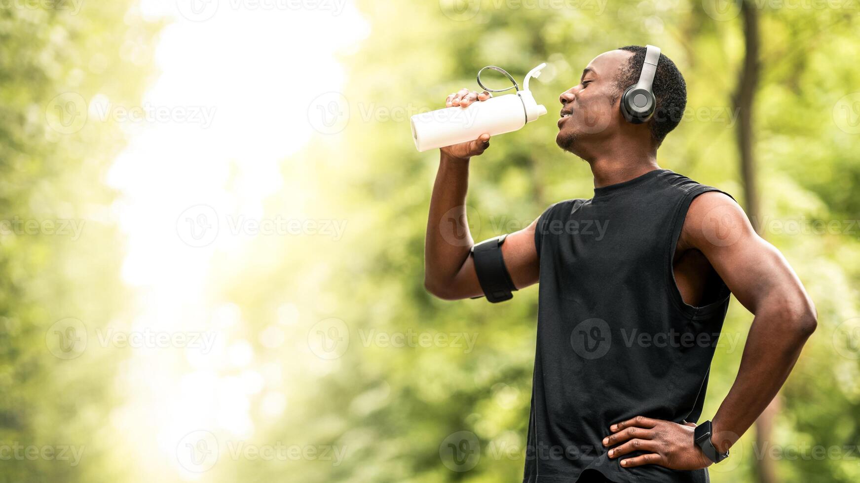 African american young sportsman drinking water, having break during exercising open air, copy space, side view photo