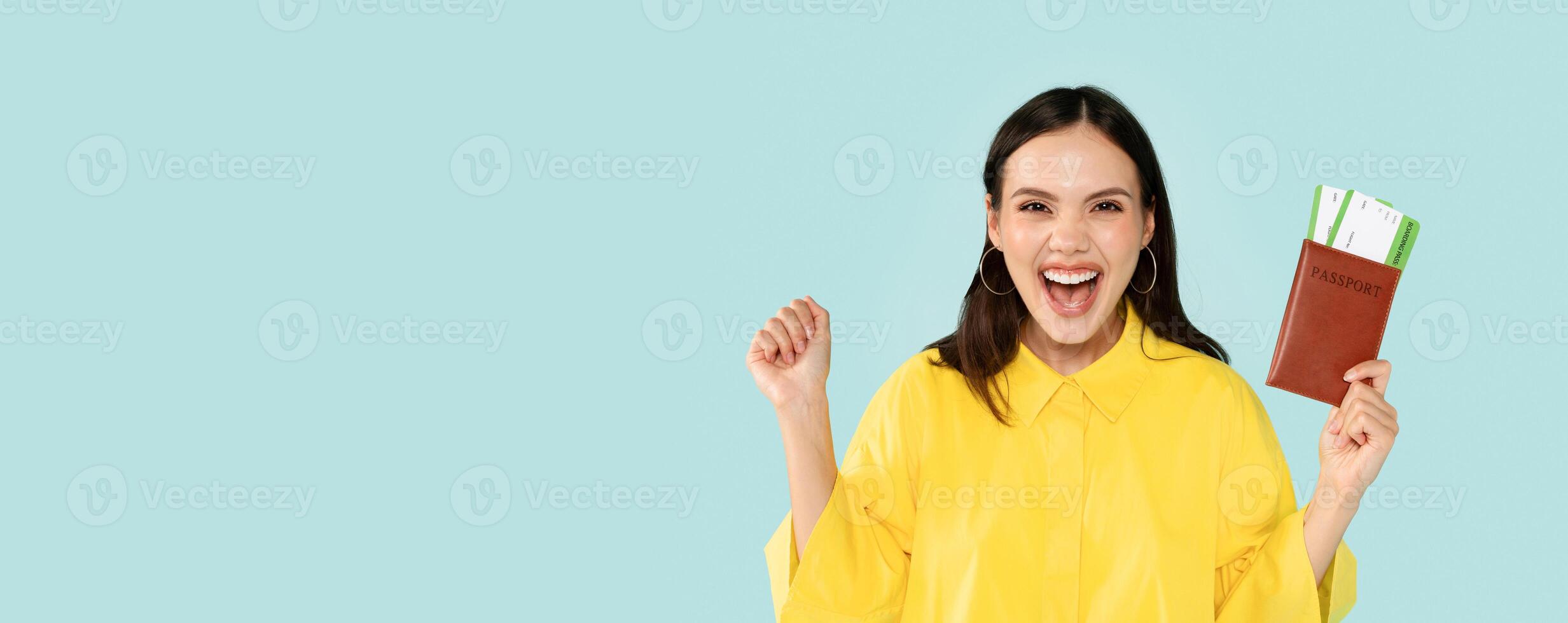 Smiling happy young woman showing passport with air tickets, clenching fist, prepare to journey, isolated over blue background, studio. Vacation, travel, people emotions and facial expression photo