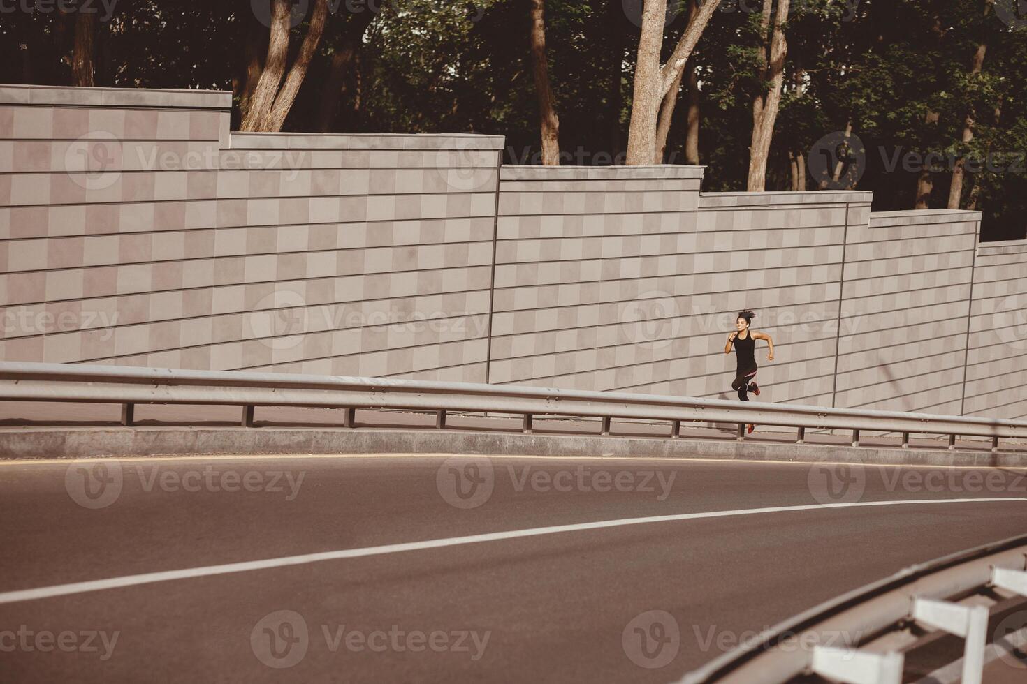 Female runner sprinting on street. African american girl in sportswear fast runs along track in city, free space photo