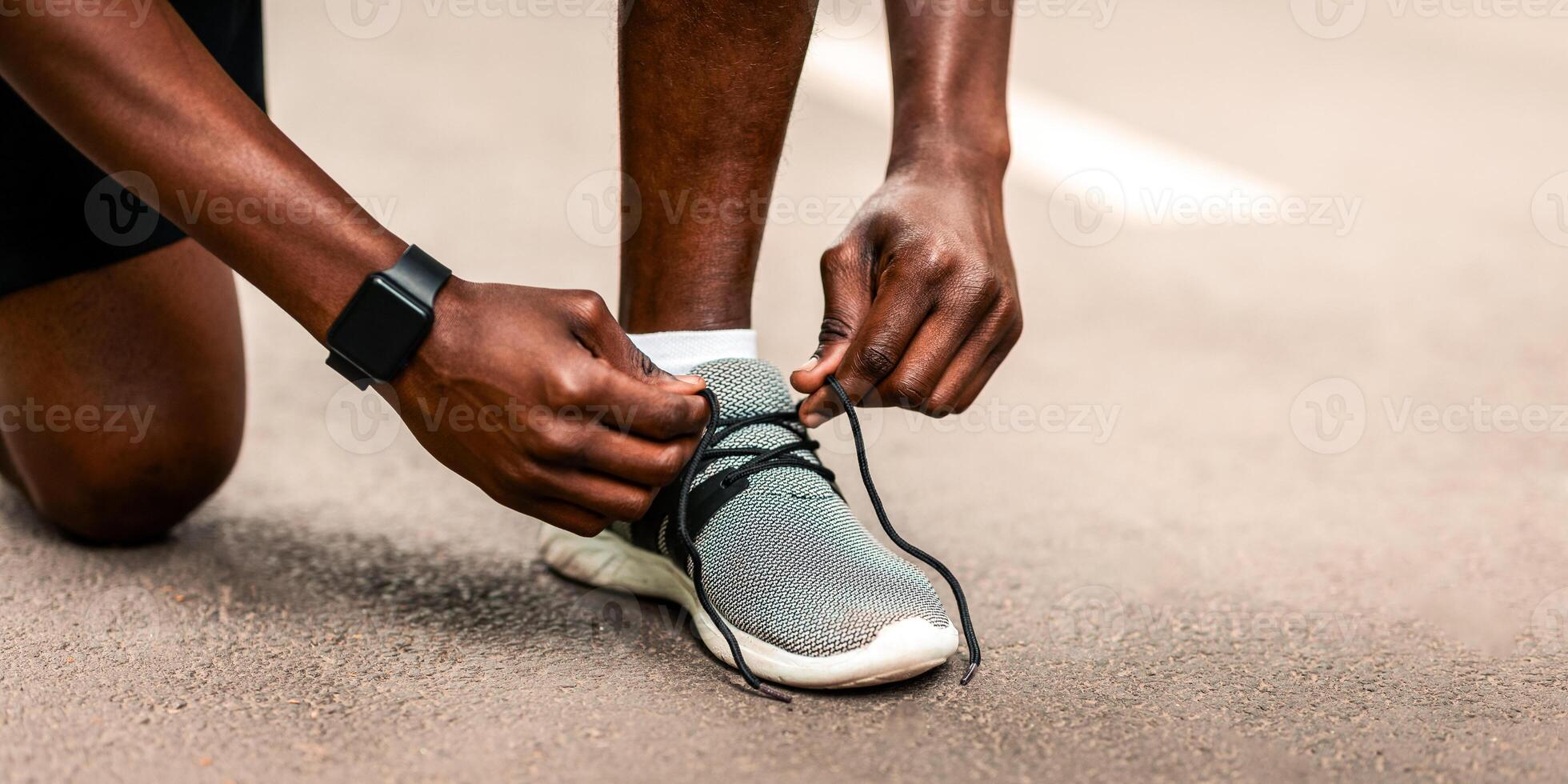 Closeup of unrecognizable black guy tying his shoelaces before jogging outdoors photo