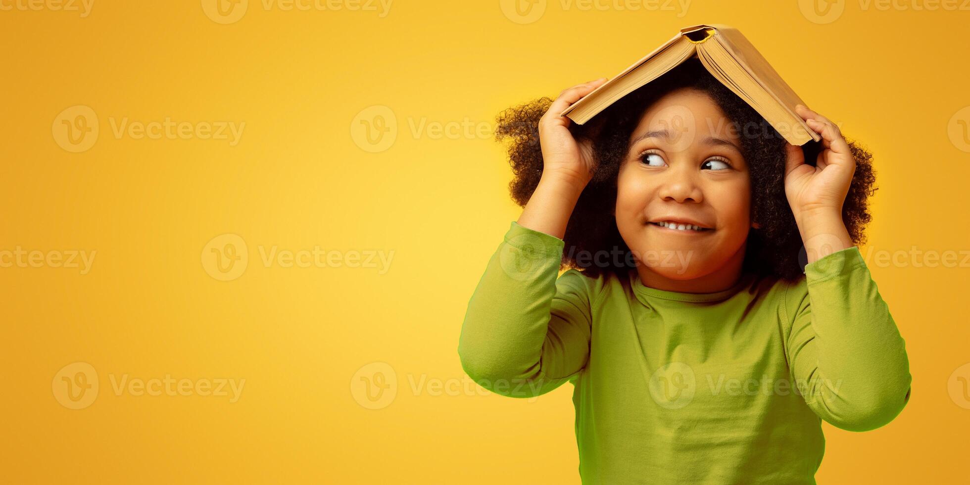 Early Education And Development. Funny Little Black Girl Hiding Under Opened Book, Isolated On Yellow Background, Panorama With Copy Space photo