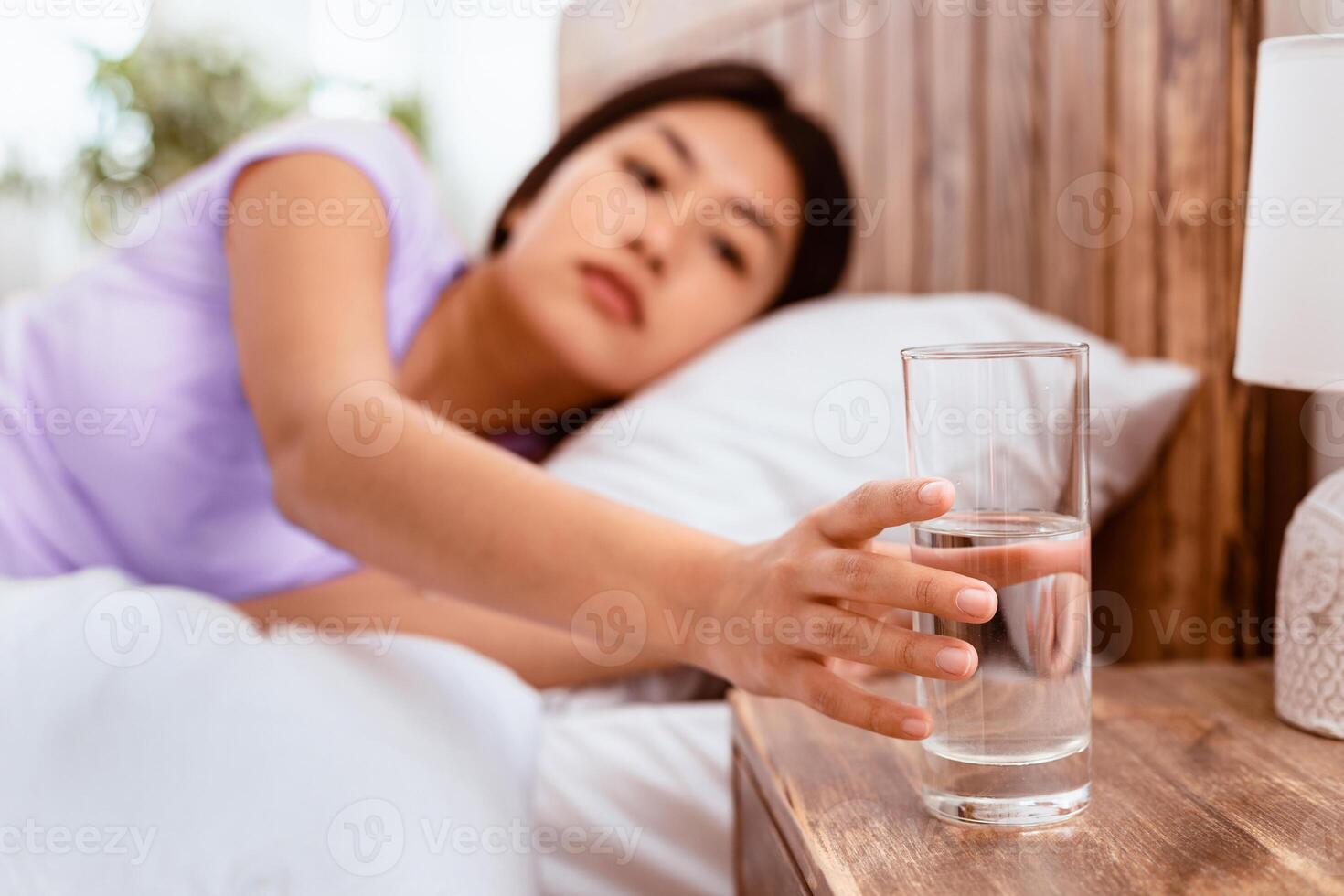 Healthy Liquid. Asian Lady Drinking Water From Glass Starting Day With Hydration Lying In Bed At Home. Selective Focus photo