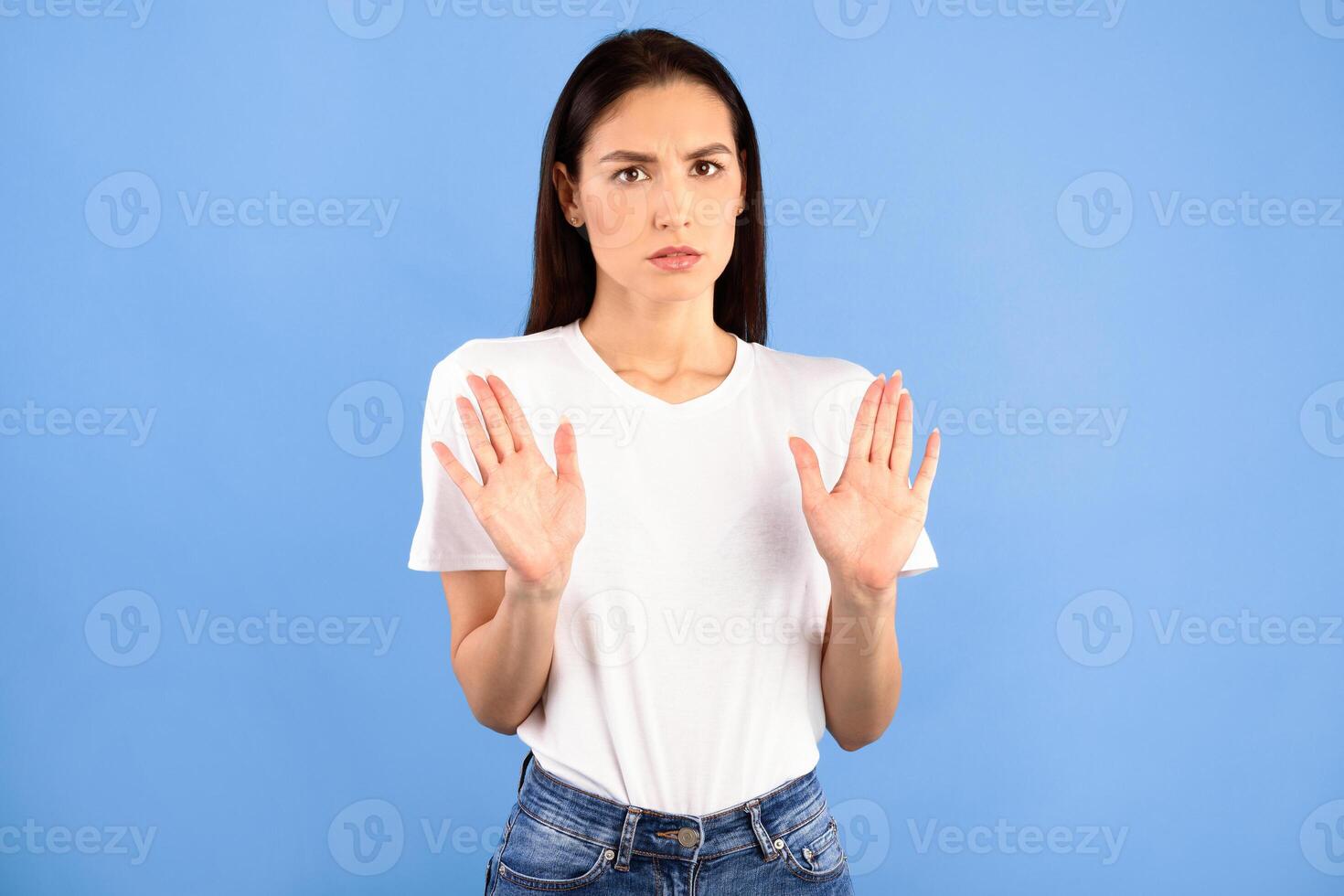 Stop Concept, Thank You But No. Portrait of serious lady making stop hand gesture, isolated on blue studio background. Displeased woman in fear showing denial sign with two palms to camera photo