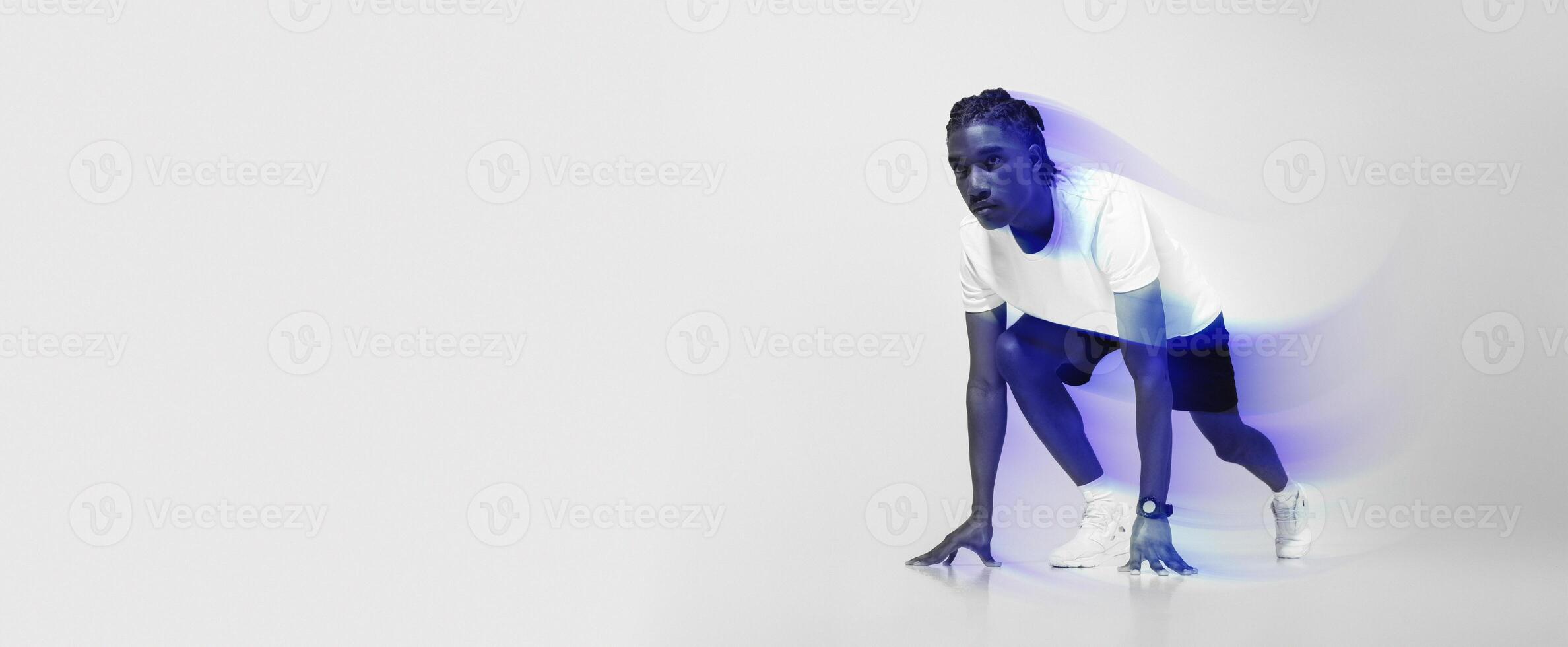 Focused man in athletic wear poised in starting position for sprint, young african american runner guy exuding determination and strength, posing on light grey studio background, copy space photo