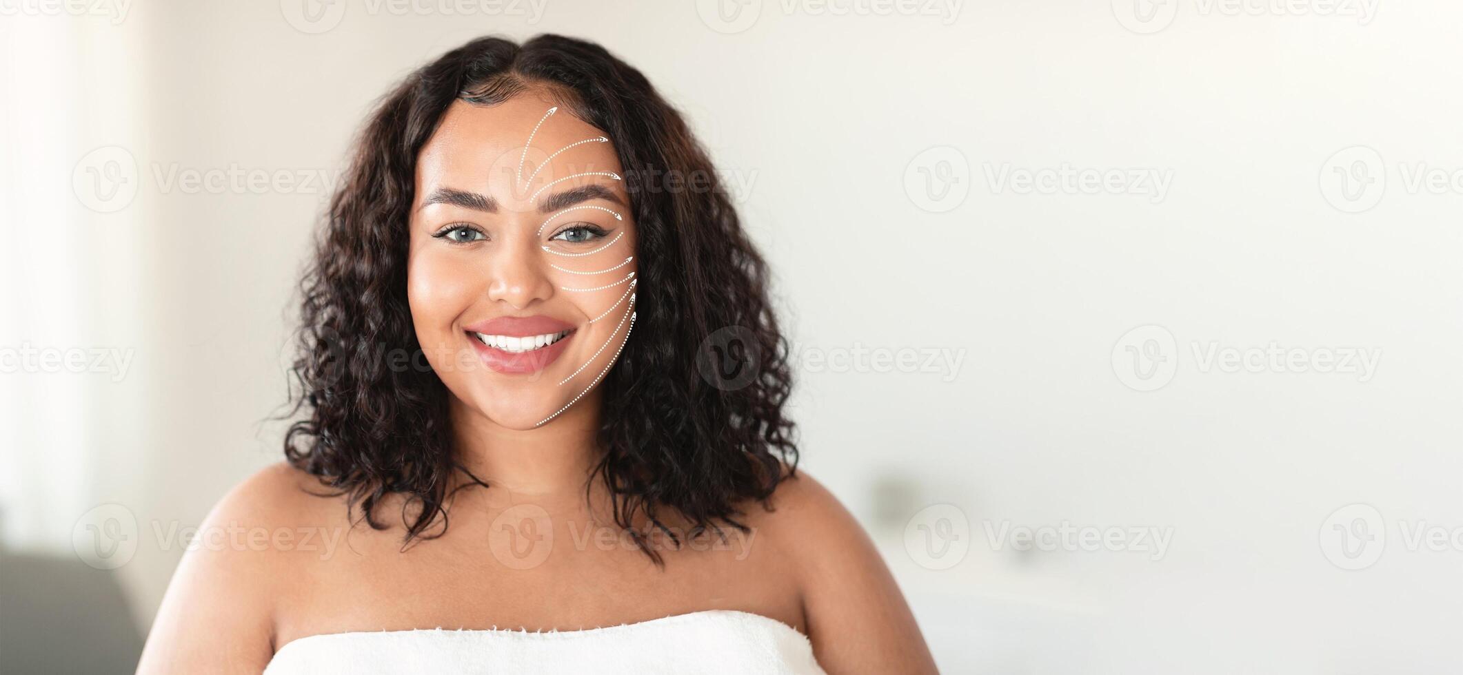 African American woman with curly hair smiles brightly while receiving a facial massage in a serene spa setting. She is pampering her skin with an anti-aging treatment focused on rejuvenation. photo